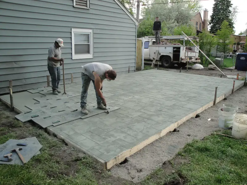 Crew pressing texture mats into a freshly poured patio next to a house