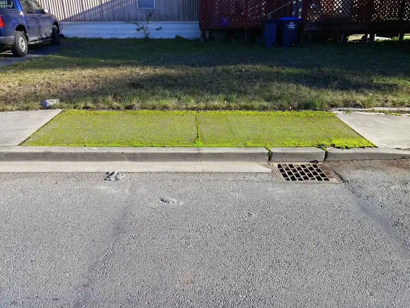 Concrete sidewalk along a lawn with a curb inlet nearby